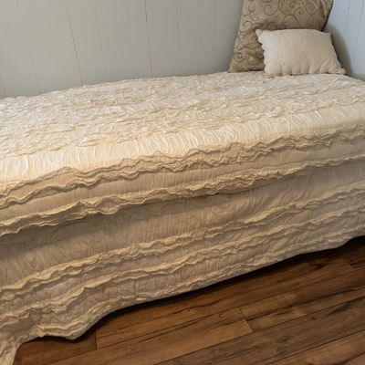 Twin bed dressed in a cream ruffled bedspread with matching bed skirt and accent pillows.