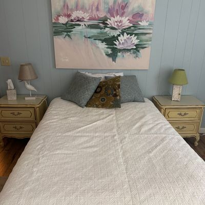 Bedroom set featuring a pair of vintage French Provincial style nightstands, small table lamps, and a large canvas painting depicting...