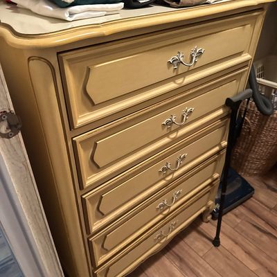 French Provincial style five-drawer tallboy dresser painted in off-white and gold accent trim with ornate metal handles.