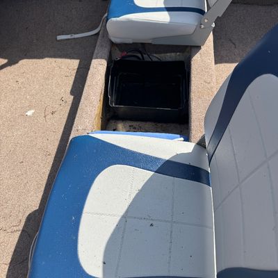 Interior of a boat featuring blue and white vinyl folding seats, carpeted floor, and an open battery compartment.