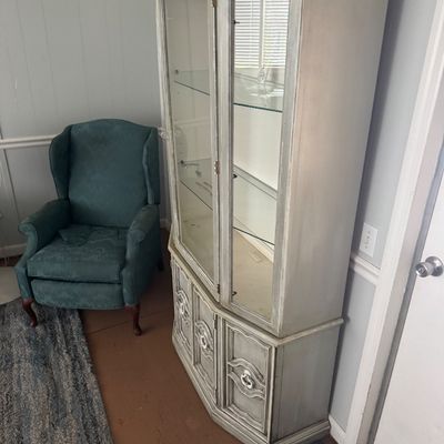 French Provincial style distressed gray-painted china cabinet with glass doors and inner shelving, paired with a teal upholstered...