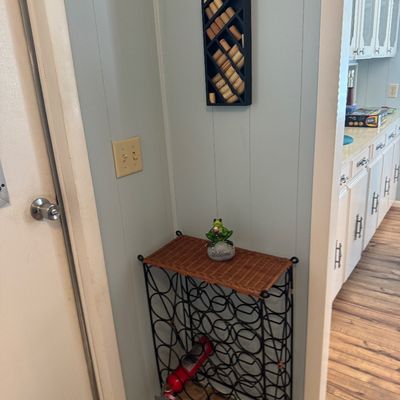 Black metal scrollwork wine rack table with a woven wicker top, paired with a wall-mounted bottle-shaped cork collector.