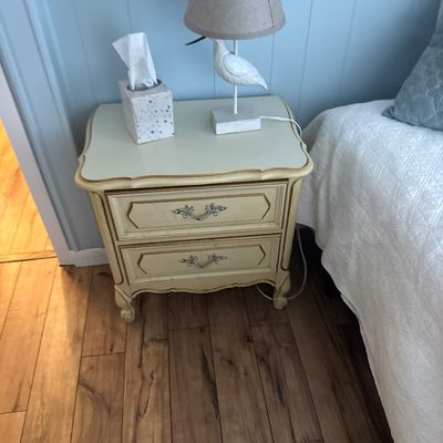 French Provincial style two-drawer nightstand in off-white paint with gold trim accents, paired with a coastal shorebird table lamp.