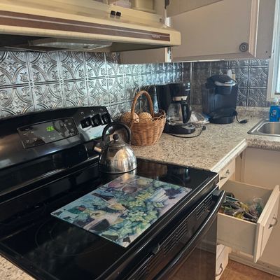 Black glass-top electric range with a stainless steel tea kettle and glass trivet, pictured along a countertop with small appliances...