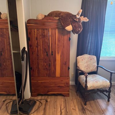 Rustic cedar wardrobe cabinet topped with a large stuffed plush moose, alongside a vintage upholstered armchair.