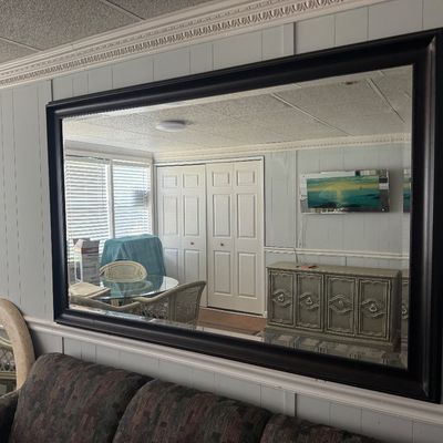 Large rectangular wall mirror with a dark molded wood frame, mounted above a sofa.