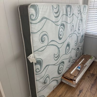 Modern full or queen-size mattress with a teal swirl pattern leaning against a wall.