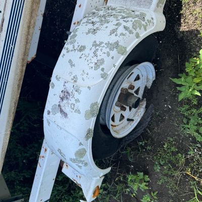 White boat trailer wheel assembly with weathered fiberglass fender and damaged flat tire.