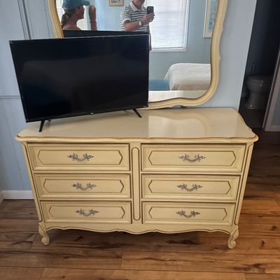 French Provincial style six-drawer dresser with cream finish, gold accents, and a matching attached wall mirror.