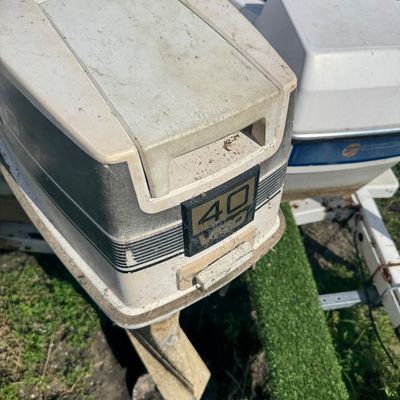 Vintage Evinrude 40 VRO outboard boat motor attached to a small fiberglass boat. The engine cowling shows weathering, dirt, and surface...