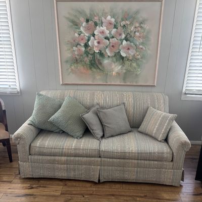 Upholstered striped sofa with rolled arms and matching throw pillows, paired with a large framed floral painting.