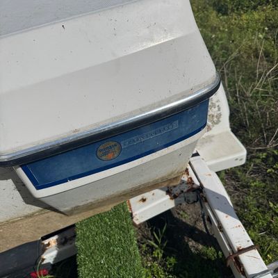Stern corner detail of a white fiberglass boat on a trailer, featuring chrome hardware and a hull identification number tag.