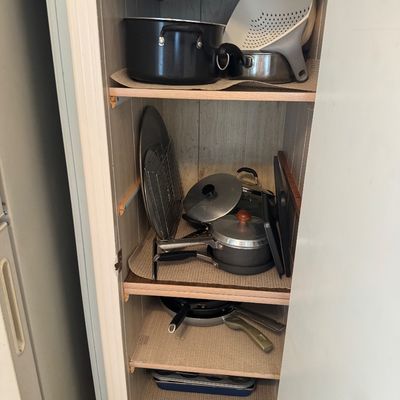 Tall narrow pantry cabinet filled with assorted cookware, including pots, pans, lids, baking sheets, and a colander.