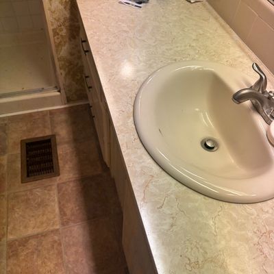 Vintage 1970s bathroom vanity with a faux-marble laminate countertop, cream-colored drop-in sink, and chrome faucet. A black hair dryer...