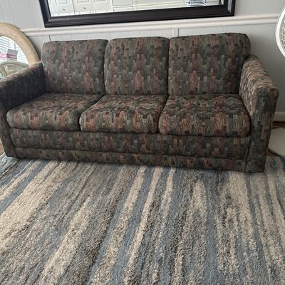 Vintage three-cushion sofa upholstered in a multi-toned geometric patterned fabric, resting on a striped area rug.