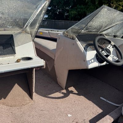 Interior view of a vintage powerboat console featuring twin windshields, steering wheel, and carpeted deck.