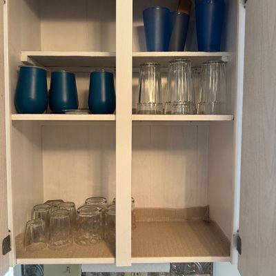 Collection of modern glassware and insulated blue travel tumblers arranged inside a white wooden kitchen cabinet.