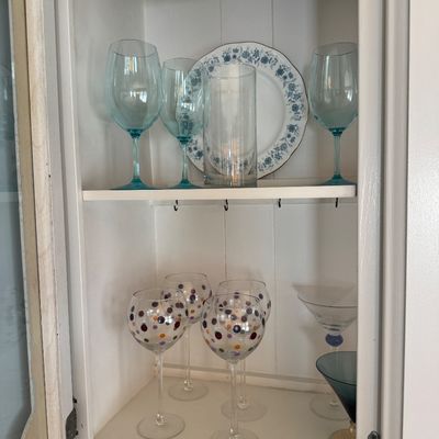 Collection of assorted glassware displayed in a white cabinet, including light blue wine glasses, polka dot balloon glasses, and martini...