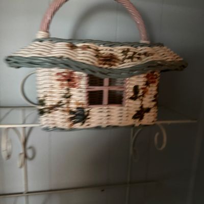Novelty cottage-shaped wicker basket purse featuring floral accents, a pink top handle, and a cutout window frame detail.