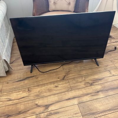 TCL flat-screen television with original stand legs, resting on a wood-look floor.