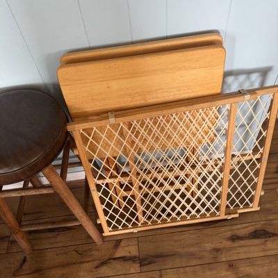 Group of household items including an expandable wooden safety gate, light wood folding TV tray tables, and a brown leatherette topped...