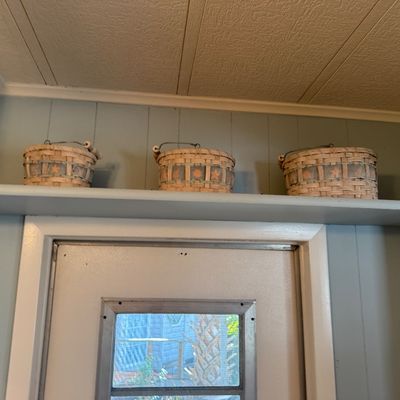 Set of three small woven baskets with decorative fabric bands displayed on a high wall shelf.