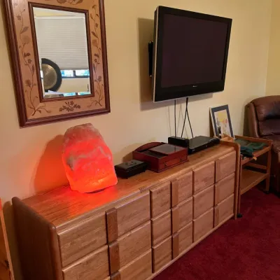 Sale Photo Thumbnail #31: Large light oak lowboy dresser featuring panel-front drawers, topped with a glowing Himalayan salt lamp, decorative boxes, and a wall-mounted flat-screen TV.
