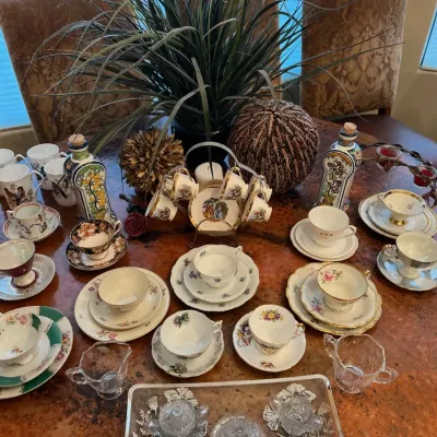 Sale Photo Thumbnail #21: Extensive collection of fine china teacups, saucers, decorative decanters, and silver overlay glassware arranged on a dining table.