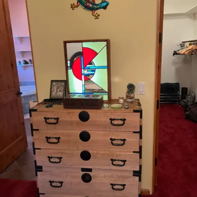 Sale Photo Thumbnail #29: Japanese tansu chest of drawers with decorative metal hardware, topped with a stained glass panel and various small decor items.