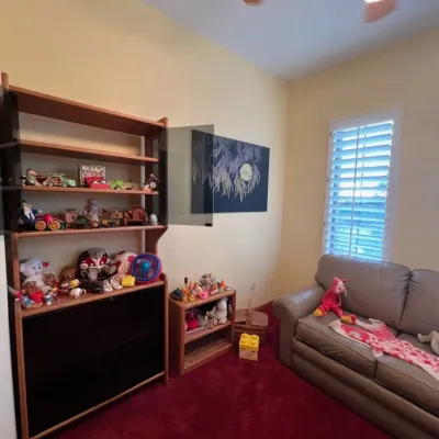 Sale Photo Thumbnail #12: A room featuring a tan leather sofa, a tall wooden bookcase with glass doors filled with plush toys and knick-knacks, and a smaller wooden shelf unit alongside a lighted ceiling fan.
