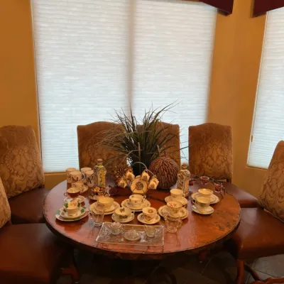 Sale Photo Thumbnail #22: Round copper-top dining table set with high-back upholstered chairs and displayed porcelain teacups with saucers.
