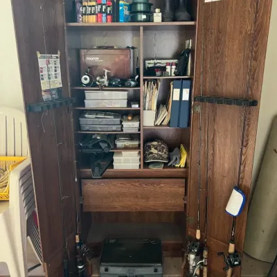 Sale Photo Thumbnail #43: Tall wood laminate fishing gear cabinet, featuring door racks for fishing rods, interior shelving packed with tackle boxes, reels, line, and a bottom drawer.