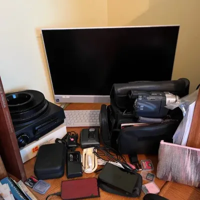 Sale Photo Thumbnail #14: Collection of vintage electronics including a Kodak Carousel slide projector, a computer monitor, a camcorder in a soft bag, and various small accessories.