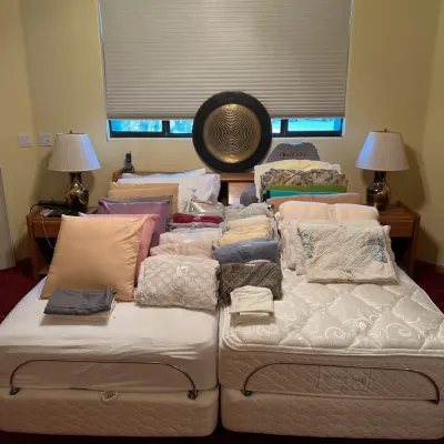 Sale Photo Thumbnail #27: Split king adjustable bed set loaded with sorted linens, pillows, and bedding, flanked by matching wooden nightstands and table lamps.