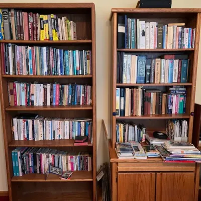 Sale Photo Thumbnail #9: Two tall oak wooden bookcases fully stocked with books, reference materials, and various literature.