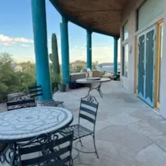 Sale Photo Thumbnail #45: Covered outdoor patio featuring wrought iron chairs and a round mosaic-top bistro table against a desert backdrop.
