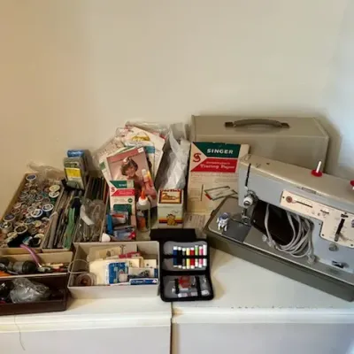 Sale Photo Thumbnail #10: Vintage beige and grey sewing machine alongside a large collection of sewing notions, spools of thread, vintage patterns, and dressmaker's tracing paper.