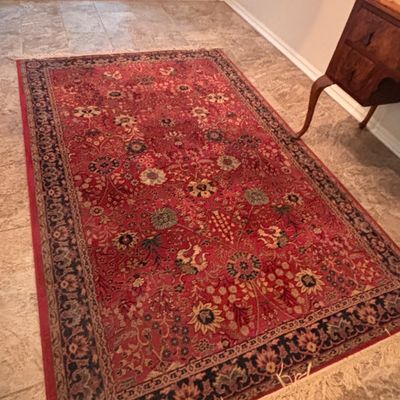 Sale Photo Thumbnail #124: Traditional Persian-style area rug featuring an ornate floral pattern in shades of red, dark blue, and cream with fringed ends.