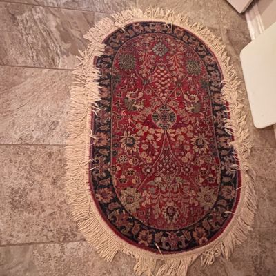 Sale Photo Thumbnail #122: Small oval oriental-style accent rug featuring a intricate floral pattern in shades of red, navy blue, and beige with long fringe trim around the perimeter.