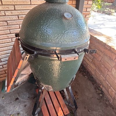 Sale Photo Thumbnail #7: Large Big Green Egg ceramic kamado grill featuring wooden side shelves and a wheeled rolling nest stand.