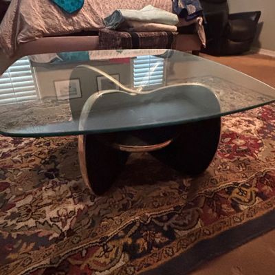 Sale Photo Thumbnail #46: Mid-century modern style glass-top coffee table with a curved dark wood and metallic base, set on an ornate traditional area rug.