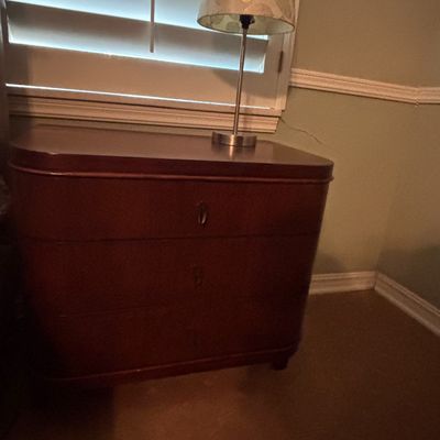 Sale Photo Thumbnail #47: Vintage dark mahogany three-drawer chest with rounded corners, topped with a modern table lamp featuring a leaf-patterned shade.