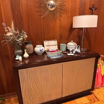 Sale Photo Thumbnail #117: Mid-century dark wood console cabinet with textured front panels, topped with various decorative ceramics, a starburst mirror, and a table lamp.