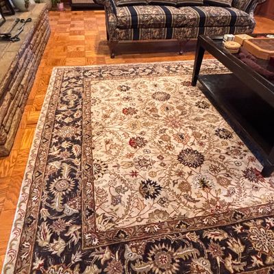 Sale Photo Thumbnail #99: Large Persian-style area rug featuring a beige field with a dark blue and brown floral border, shown alongside a striped floral sofa in a living room.