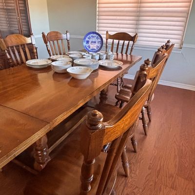 Sale Photo Thumbnail #148: Traditional oak dining table with matching spindle-back chairs, set with porcelain dinnerware and a decorative blue and white collector plate.