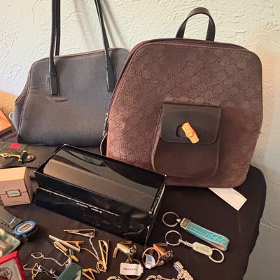Sale Photo Thumbnail #159: Collection of accessories including a brown GG canvas backpack with bamboo turn-lock detail, a grey shoulder bag, vintage keychains, tie clips, and small boxed items.