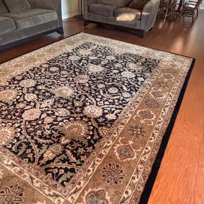Sale Photo Thumbnail #151: Large Persian-style area rug featuring a dark navy floral central field surrounded by an ornate beige and tan border.