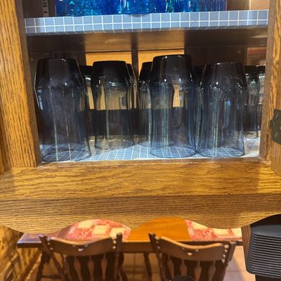 Sale Photo Thumbnail #218: Collection of vintage glassware stored in a wooden cabinet, including smoke grey highball glasses and bright blue textured tumblers.