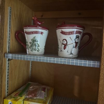 Sale Photo Thumbnail #235: Pair of holiday-themed ceramic covered mugs featuring snowmen and pine trees with cardinal lids, displayed in a wooden cabinet.