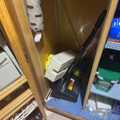Sale Photo Thumbnail #241: Assorted household cleaning supplies, including a broom, dustpan, and caddy, stored in a wooden cabinet.